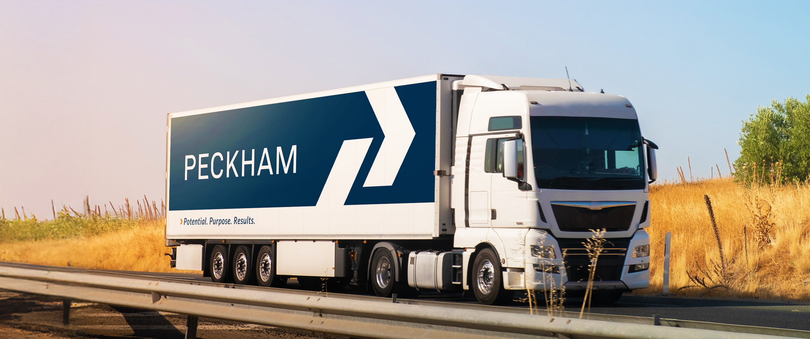 A semi-truck displays the Peckham logo, in white font in front of a blue background. 