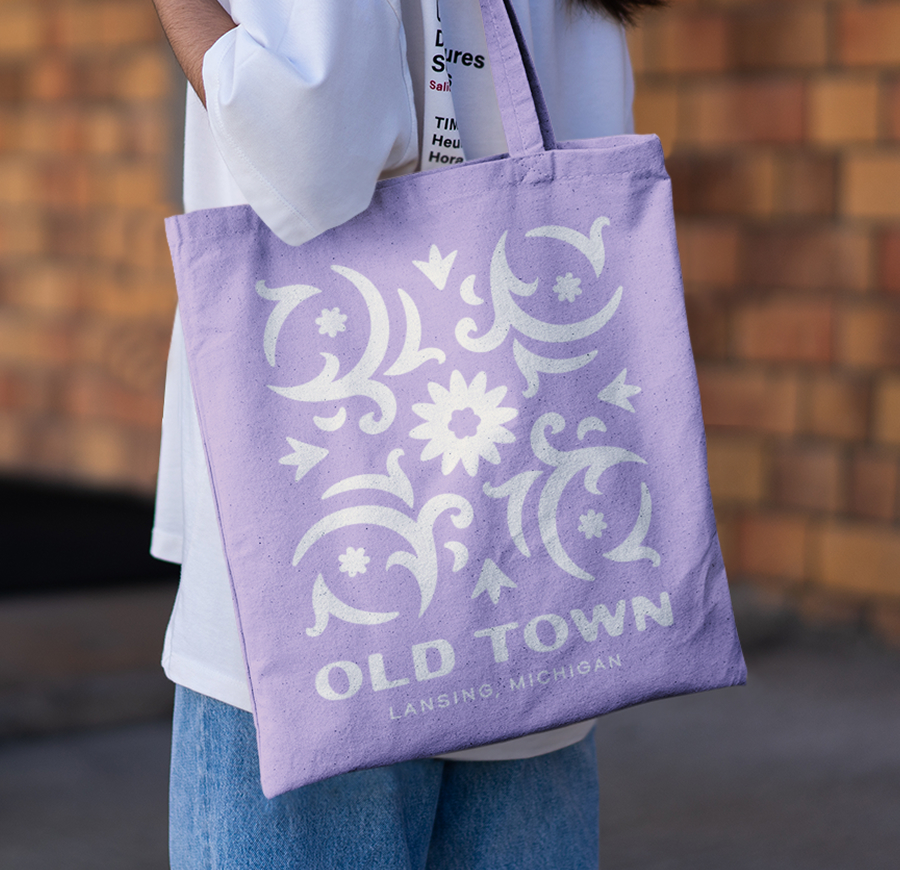 Light purple tote with branded floral decoration and "Old Town Lansing, Michigan" below it.